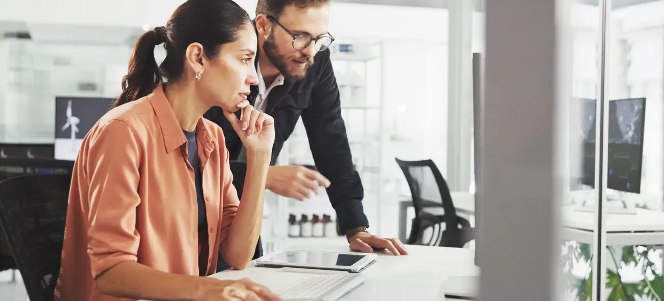 Windkraftflächen erfolgreich sichern: Strategien für Projektentwickler in einem dynamischen Markt Zwei Personen betrachten im Büro Dokumente zu Windkraftflächen auf einem Monitor.