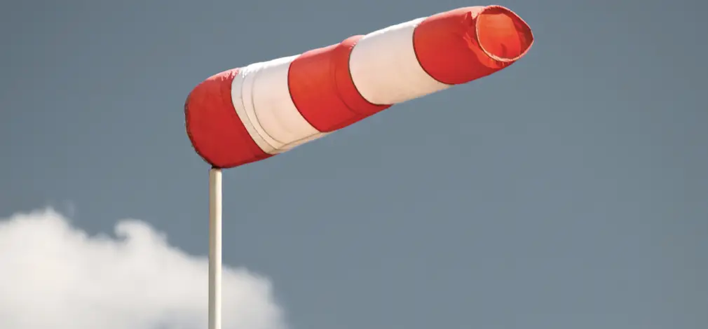 Windsack weht vor hellblauem Himmel und steht für Windmessung.