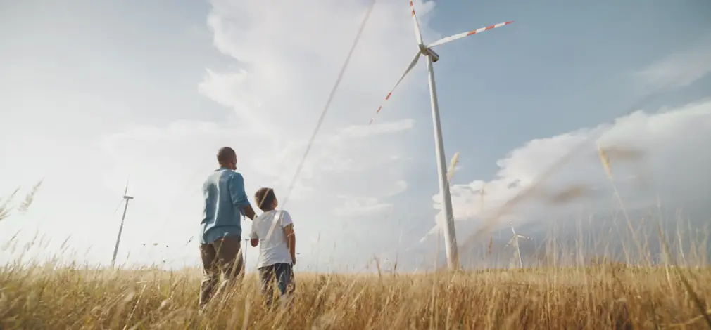 Mann steht mit Kind auf einem grünen Feld, beide blicken zu einem Windrad, da sie einen Pachtvertrag für die Windkraftanlage besitzen. Mann steht mit Kind auf einem grünen Feld, beide blicken zu einem Windrad, da sie einen Pachtvertrag für die Windkraftanlage besitzen.