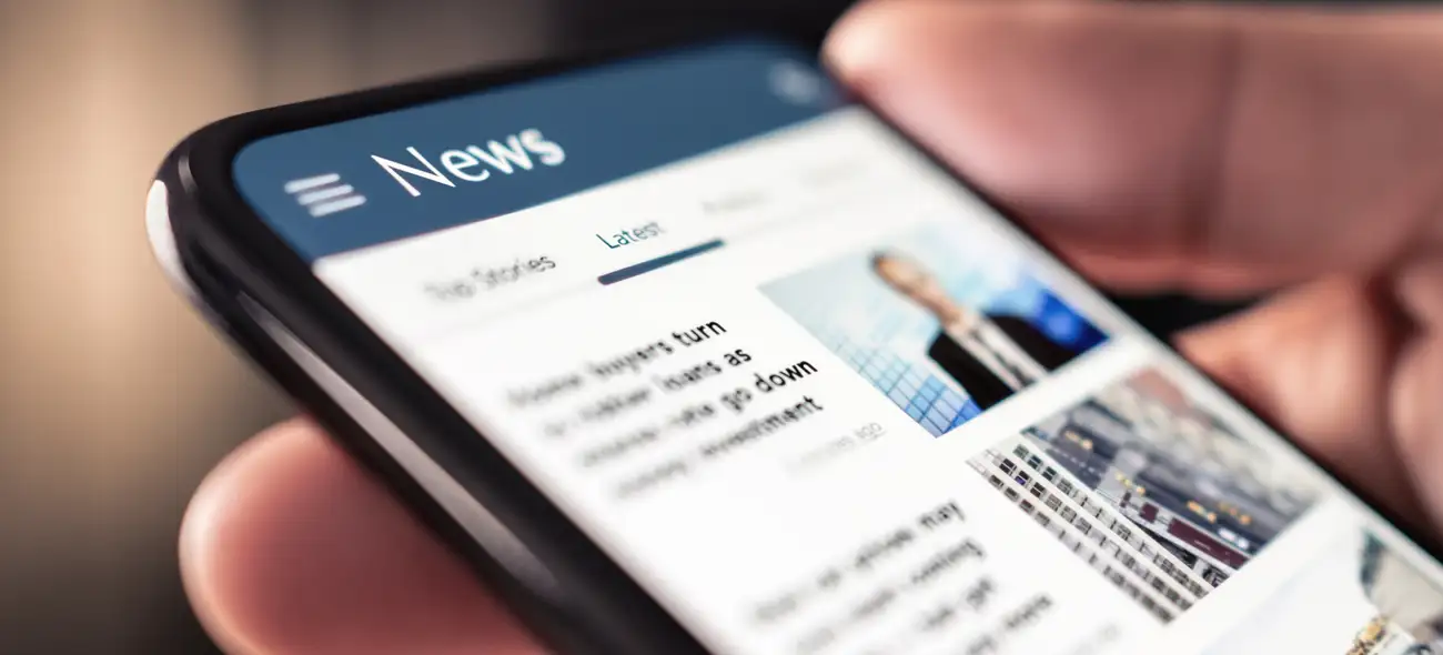 Hand hält Smartphone mit geöffneter News-App.