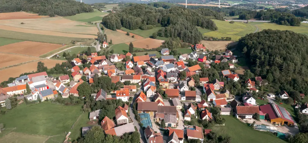 Luftaufnahme eines Dorfes mit mehreren Windrädern in hügeliger Landschaft im Hintergrund. Luftaufnahme eines Dorfes mit mehreren Windrädern in hügeliger Landschaft im Hintergrund.