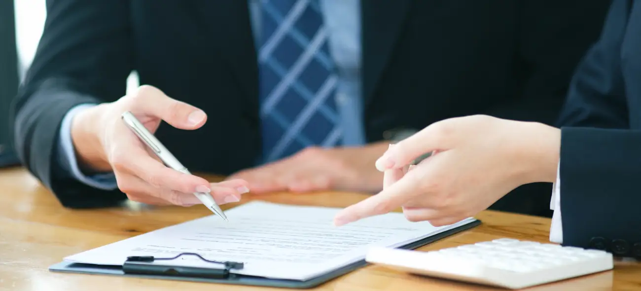 Windkraft-Pachtvertrag: So gestalten und verhandeln Sie erfolgreich Zwei Personen sitzen am Tisch, eine Person hält einen Stift über einem Vertrag zum Windkraft-Pachtvertrag.