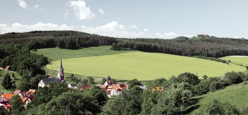 Blick auf ein Dorf mit Kirche inmitten einer hügeligen, grünen Landschaft. Blick auf ein Dorf mit Kirche inmitten einer hügeligen, grünen Landschaft.