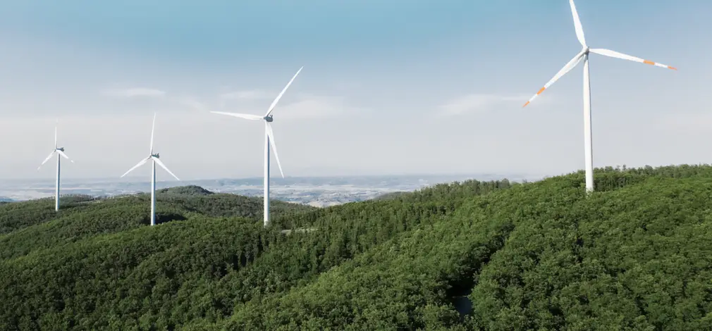 Vier moderne Windräder auf bewaldeten Hügeln unter blauem Himmel. Vier moderne Windräder auf bewaldeten Hügeln unter blauem Himmel.