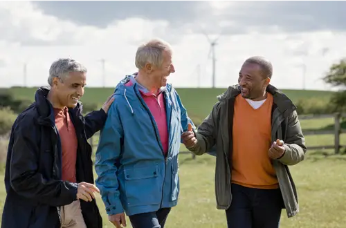 Drei Männer gehen über eine Ackerfläche im Saarland mit Windpark im Hintergrund.