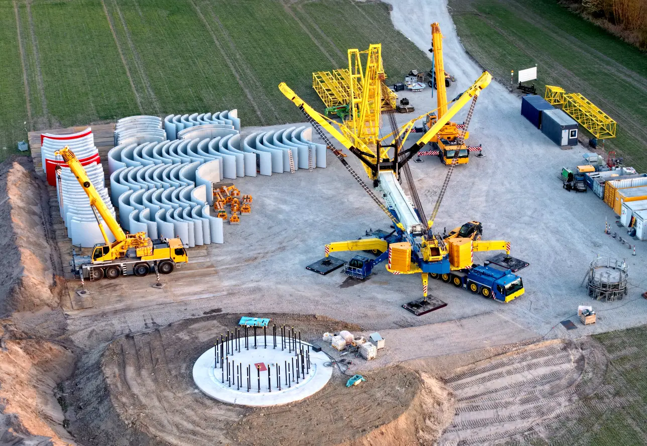 Mit der Größe moderner Anlagen steigen auch Anforderungen an Bau, Kranflächen und Logistik. Montageplatz einer Windkraftanlage mit Kran und Bauteilen.