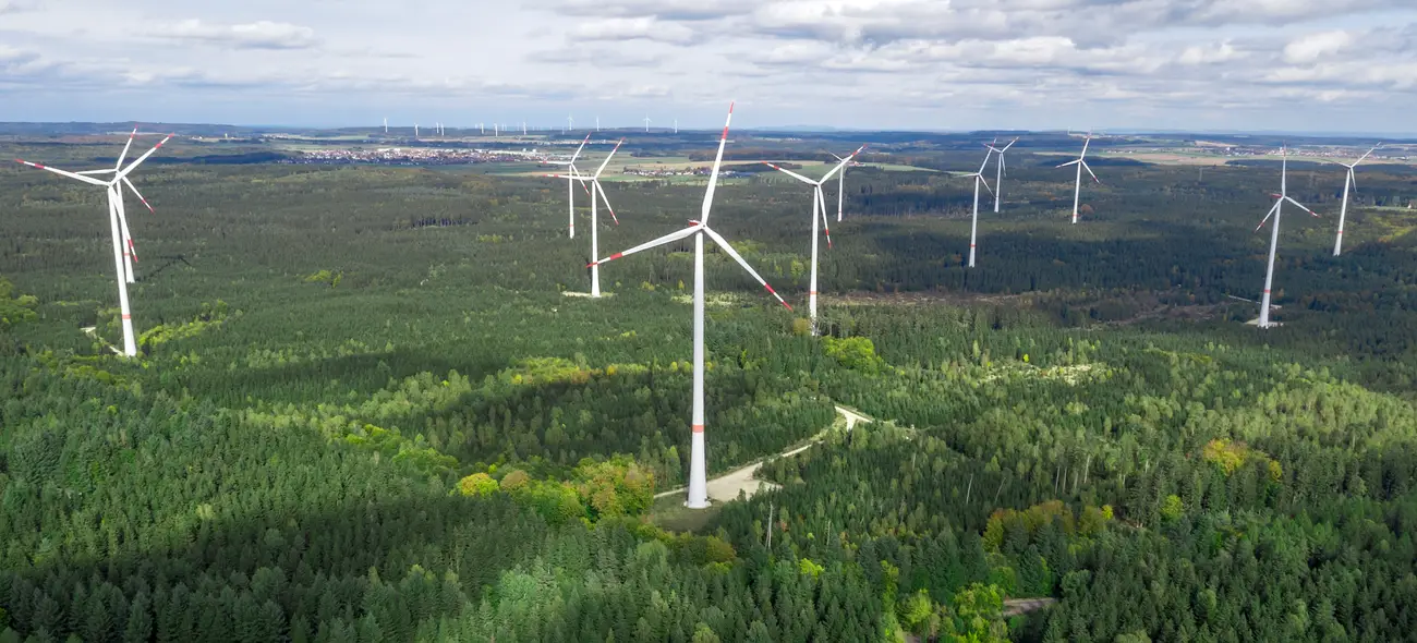 Argumente gegen Windkraftanlagen im Wald – zwischen Mythen und Fakten Windpark in einer bewaldeten Landschaft, Windräder ragen über die Baumwipfel.